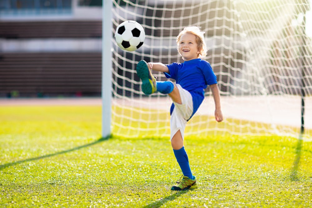 young kid kicking soccer ball in front of a soccer goal